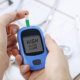 Hand holding a blood glucose meter measuring blood sugar, the background is a stethoscope and chart file